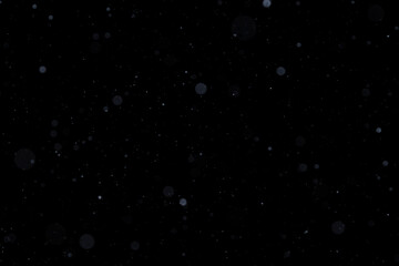 Real falling white snow against black night sky in the winter. Snowing at dark. Abstract multi-layered bokeh effect.