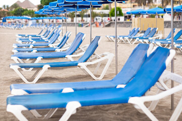 Perspective view on blue sunbeds and umbrellas on empty beach, summer cloudy day