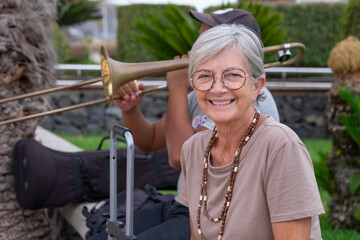 Elderly Caucasian woman sitting outdoors near a trumpet trombone player enjoying the music