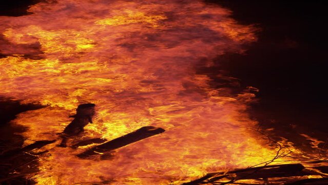 SLOW MOTION, VERTICAL, CLOSE UP: Close up view of a big campfire burning on a quiet summer night. A pile of firewood is engulfed in a fiery blaze near a quiet campsite. Scenic shot of a bonfire.