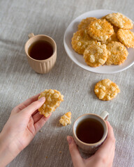 Cheese biscuits in one hand and a broken piece and a mug of coffee in the second, in the background a plate with biscuits blurred on a linen napkin