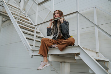 Bored longing teenager girl with dreads sitting on a steel stairs