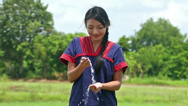Asian girl in traditional dress stands in a field and pour a rice from hand to hand