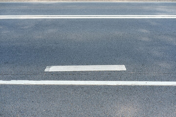 Road markings on an asphalt road, painted with white paint, damaged and chipped in places.