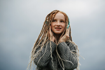 Dreamy eyed teenage girl with dreads listening music, holding headphones.