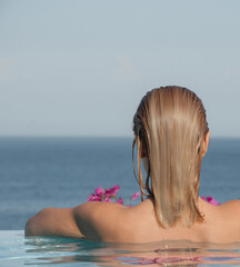 A girl with wet hair in the pool, looking at the sea in the distance.