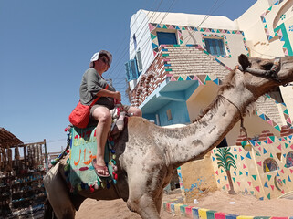 Middle aged tourist riding a camel on a nubian village in Egypt