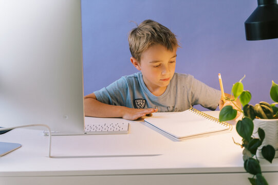 boy writing with a pencil while at the computer desk in his room