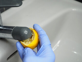 Half a lemon, a gloved hand and a chrome faucet on the sink
