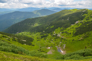 Fototapeta na wymiar Panoramic aerial view of small mountain lake in the valley between the green slopes of the mountains. Carpathians, Ukraine 