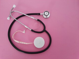 Stethoscope with a tape measure on a pink background. disease obesity.