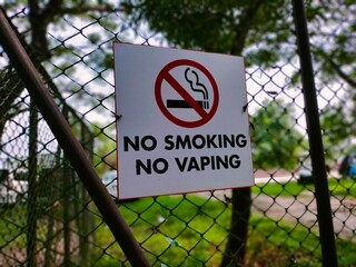 Close up of a no smoking, no vaping sign fixed on metal chain fence in front of school playground...