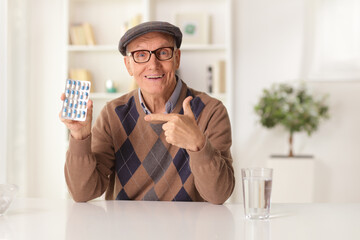 Elderly man sitting at home and pointing at a pack of pills