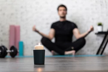 Fotobehang Close-up of candle with practicing yoga in lotus pose man on background. Yoga poses and stretching concept © Vitaliy