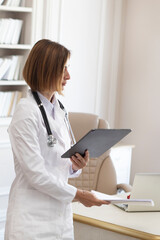 Side view on female physician standing and holding gadget and documents of patients. Modern health care concept