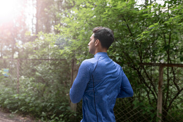 Side view on handsome man in blue sportswear jogging in the wood at the morning time