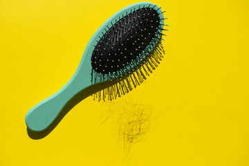 Green comb and fallen hair on the yellow background. Baldness and hair loss problem