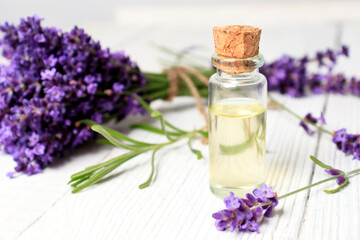 Obraz na płótnie Canvas A bottle of essential oil and a bouquet of fresh lavender flowers on a white wooden background. A set of spa treatments and aromatherapy.