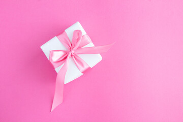 Gift box with tied pink bow on the pink background. Closeup. Top view.