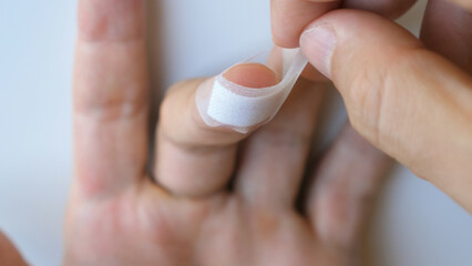 Man putting medical adhesive tape waterproof sticking plaster on cuts wound on finger. Male applying band aid patch to injured sore fingers. First aid after accident, self cure concept. Close-up.