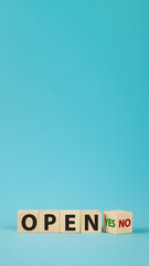 The word OPEN is written on wooden cubes. The hand turns the wooden cube and changes the word NO OPEN to YES OPEN