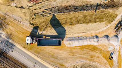 Aerial view on tipper truck is unloading gravel from trailer over construction site for new traffic...