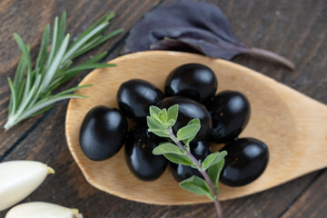 olives with spices and rosemary in a wooden spoon