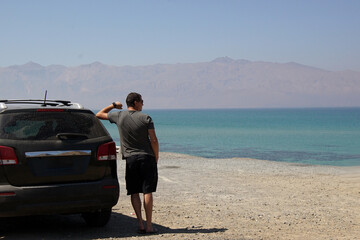 Lonely man stands near car parked at the blue sea.