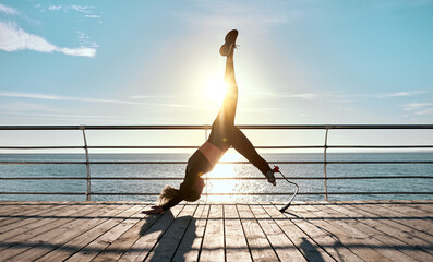 Sports training of a woman with a prosthesis on a bridge with a view of the sea and sunrise. The concept of strength, training, yoga, pilates.