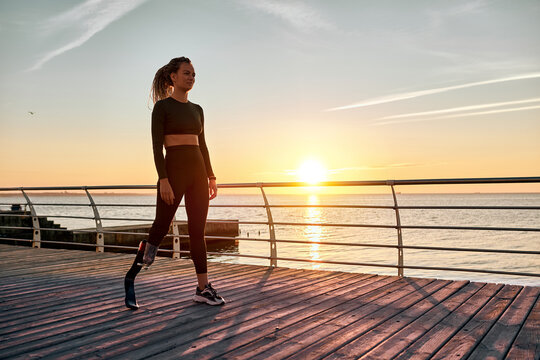 A sports woman with a prosthesis stands on the bridge in the morning at sunrise. Copy space.