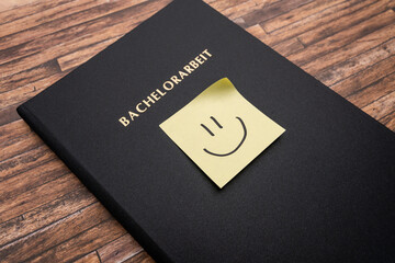 Adhesive note with a smiley on a Bachelorarbeit (bachelor thesis). Printed and bound thesis with a black cover. Finishing studies in Germany and becoming a graduate student.