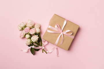Gift box and rose flowers on color background, top view