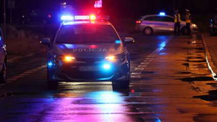 Incydent policji wieczorem w mieście.  - Sygnalizator błyskowy niebieski na dachu radiowozu policji polskiej w nocy. © FotoDax
