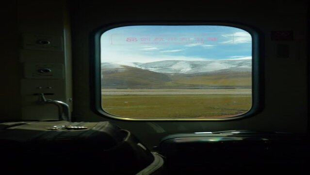VERTICAL CLOSE UP: Breathtaking view of scenic landscape of Tibet through small window in luggage compartment of sleeper train crossing China. Small window offers a view of snowy Himalaya and plains.