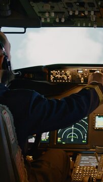 Vertical video: Diverse team of captain and copilot using dashboard command to takeoff and fly airplane. Pushing buttons to switch altitude and longitude on control panel in cockpit. Handheld shot.