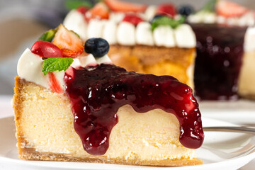 Portion of red fruit cheesecake, cream, garnished with pieces of fresh fruit strawberries, blueberry, cherry and mint