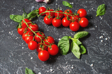 Fresh cherry tomatoes and basil with spices on a black stone background