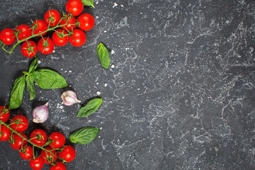 Fresh cherry tomatoes and basil with spices on a black stone background . Top view