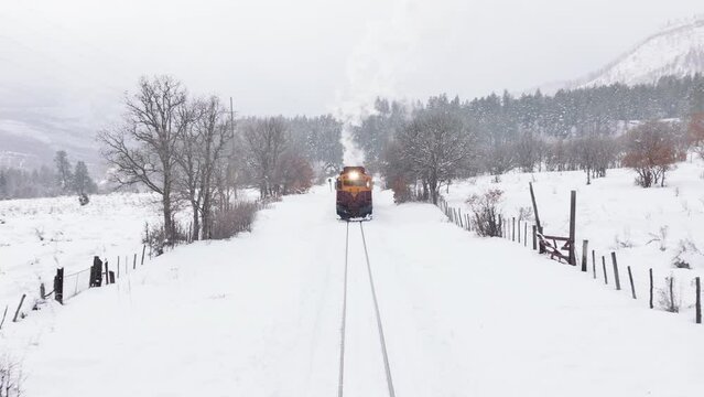 Aerial cinematic steam train moving straight to camera. Exciting railroad tour by old historic train carriages. Inspiring travel, tourists exploring winter forest on motivational adventure vacation 4K