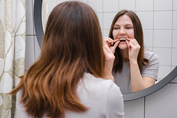 A woman in front of a mirror in the bathroom holding invisible plastic teeth aligners in hands and...