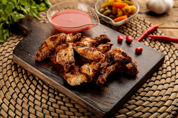 GRILLED CHICKEN WINGS with sauce and pickle served in a wooden cutting board isolated on wooden table background side view of appetizer