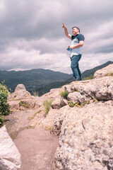 Medium build middle aged adult pointing to the sky on top of a boulder