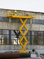 Yellow self propelled scissor lift in action with worker in uniform and safety protective equipment - obrazy, fototapety, plakaty