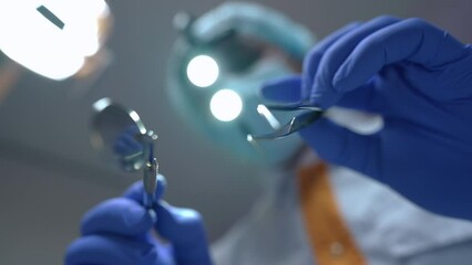 Close-up dental mirror and tweezers in hands of blurred unrecognizable doctor at background. Patient point of view of professional expert dentist with tools in hospital indoors. Slow motion