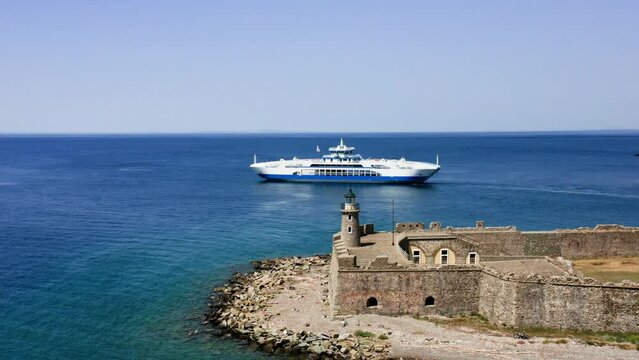 Aerial drone shot of Antirrio fortress with lighthouse and ferry boat passing by on background.