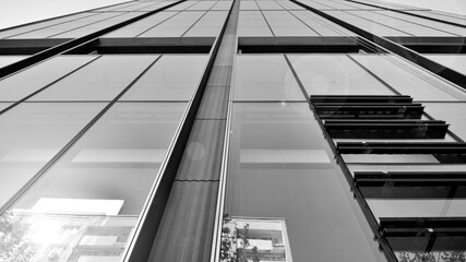 Obraz premium Bottom view of modern skyscraper in business district against blue sky. Looking up at business buildings in downtown. Rising sun on the horizon. Black and white.
