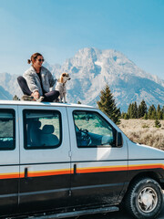 Woman and dog in matching sweaters sitting on top of a van in nature with mountain background © Kathryn
