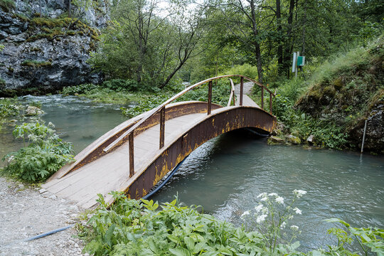 The tourist route passes through a bridge over a mountain stream, a wooden bridge with railings, a rock by the water, a trail in the forest, a place for walking on foot.
