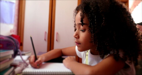 Ethnically diverse little girl child writing notes with pen. kid studying at home doing homework