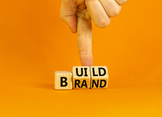Build your brand symbol. Concept words Build brand on wooden cubes. Businessman hand. Beautiful orange table orange background. Build your brand and business concept. Copy space.